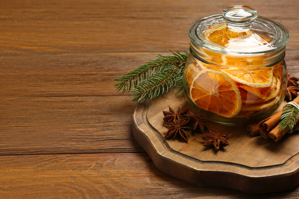 Glass jar of dry orange slices, anise stars, cinnamon sticks and fir branches on wooden table. Space for text - Fotografie, Obrázek