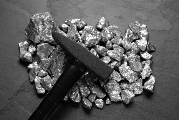 Pile of silver nuggets and hammer on black table, top view - Photo, image