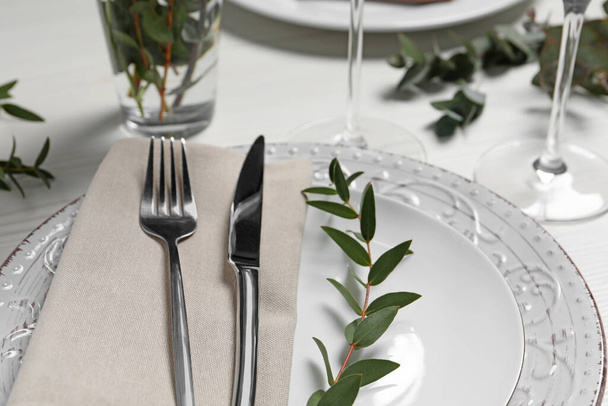 Stylish setting with cutlery and eucalyptus leaves on white wooden table, closeup - Valokuva, kuva