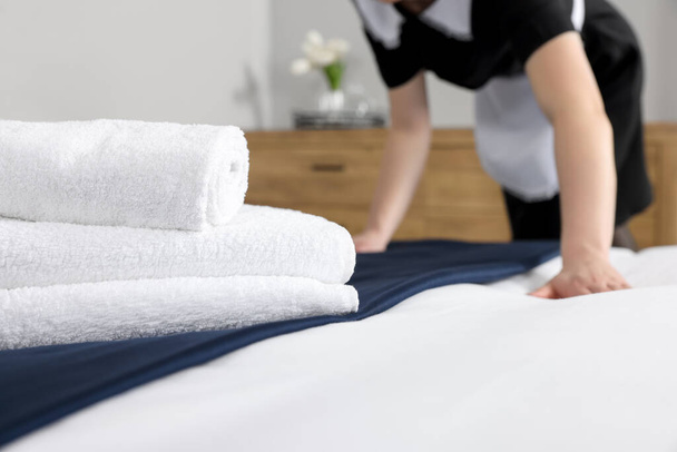 Maid making bed in hotel room, closeup. Focus on towels - Fotografie, Obrázek