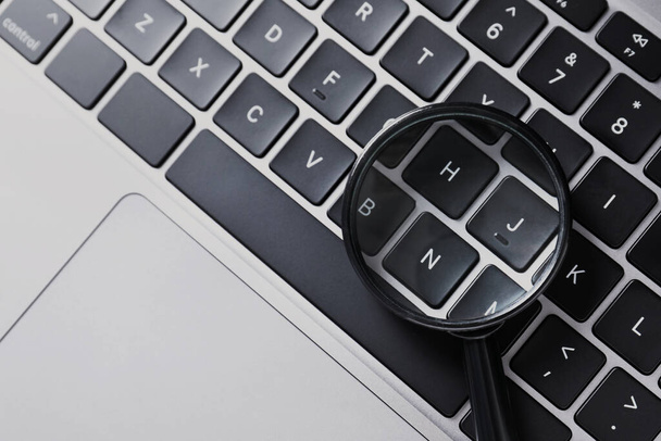 Magnifying glass on keyboard of laptop, top view - Fotografie, Obrázek