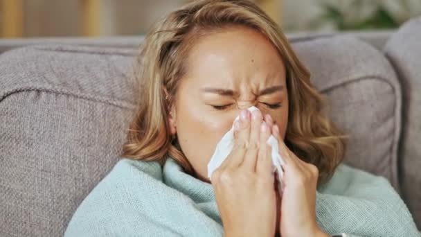 Kranke asiatische Frau, die zu Hause wegen Allergie, Covid-Virus und Sinusitis-Erkältung die Nase pustet. Niesen, Grippe und Allergien des weiblichen Gesichts auf der Couch bei der Erholung von Gesundheitsproblemen, Krankheiten und Heuschnupfen. - Filmmaterial, Video
