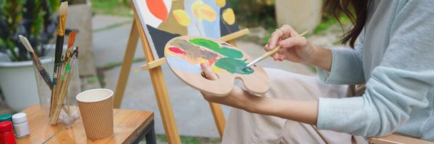 アーティストのコンセプト、女性アーティストは庭でキャンバス上の絵のためのパレット上の色を混在させるためにブラシを使用. - 写真・画像