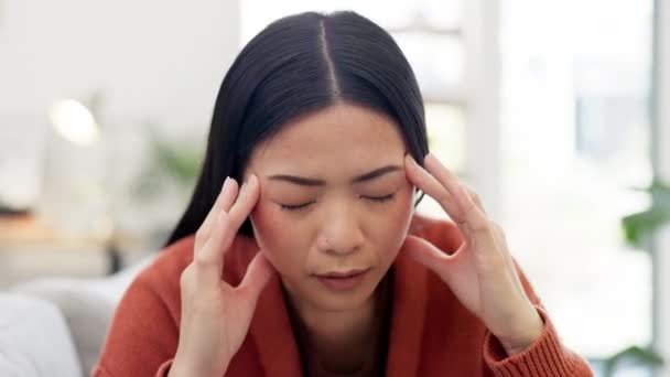 Kopfschmerzen, Stress und Burnout bei einer Asiatin im Wohnzimmer ihres Hauses, die unter Schmerzen leidet. Psychische Gesundheit, Angst oder Migräne, wenn eine junge Frau ihren Kopf hält, während sie in einem Haus atmet. - Filmmaterial, Video