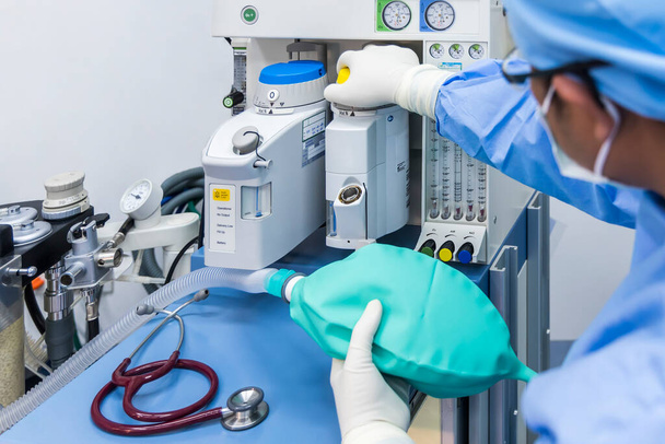 Anesthesiologist or doctor in blue gown working with anesthetic machine inside operating room in hospital.Right hand control machine with ambu bag.Medical device for surgery.Gas exchange control. - Foto, Imagen
