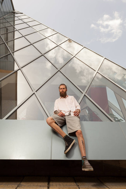 Bearded tattooed hipster posing in front of office building. Modern start up company - Fotó, kép