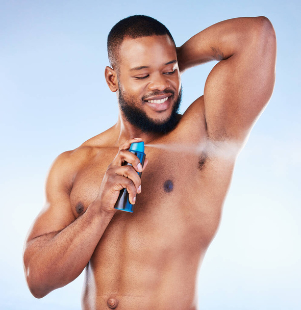 Deodorant, spray and black man with smile in studio for beauty, grooming and body hygiene on blue background. Skincare, health and male spraying aerosol, fragrance and scent product for underarm. - Photo, Image