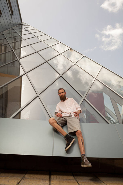 Cool bearded tattooed hipster posing in front of office building. Modern start up company - Zdjęcie, obraz