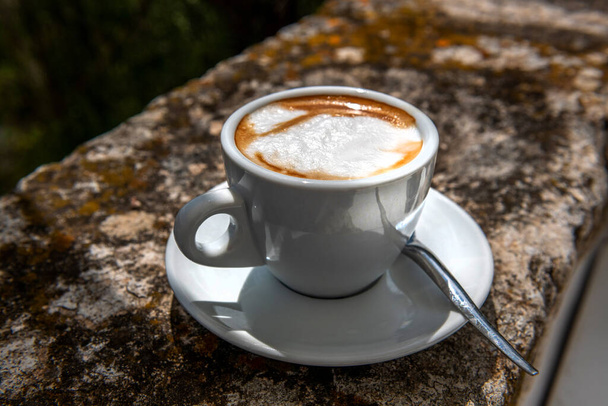 Capucino da tarde, com leite fresco, servido em um copo branco, iluminado pelos raios de sol da Itália - Foto, Imagem