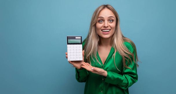 europees aangenaam verbijsterd stijlvol blond meisje met een calculator op een blauwe achtergrond. - Foto, afbeelding