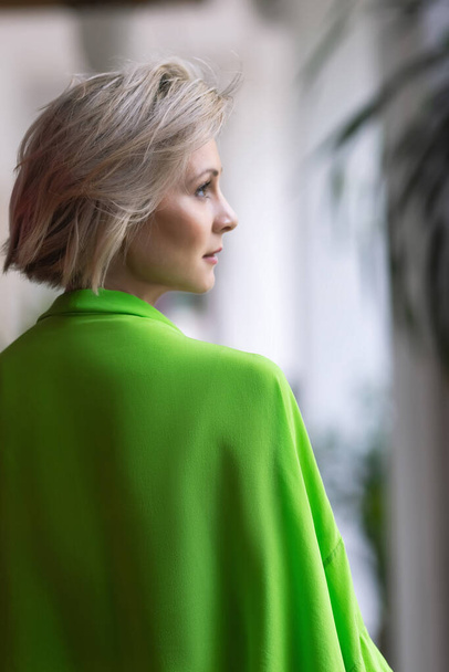 Valkoihoinen blondi kirkkaan vihreissä muodikkaissa vaatteissa aiheuttaa kameran edessä. Kampaus on houkutteleva kampaajille ja stylisteille. Laadukas kuva - Valokuva, kuva