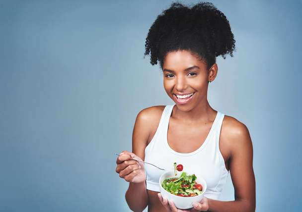 En koskaan kyllästy salaattiin ruokalistalla. Studio kuva houkutteleva nuori nainen syö salaattia harmaata taustaa vasten - Valokuva, kuva