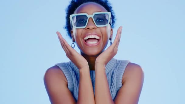 Fekete nő, napszemüveg és arc a stúdióban boldog, izgatott és divat meglepetés a kék háttér. Gen z lány, szemüveg vagy árnyalatok látás, portré és boldogság tartozék háttér. - Felvétel, videó