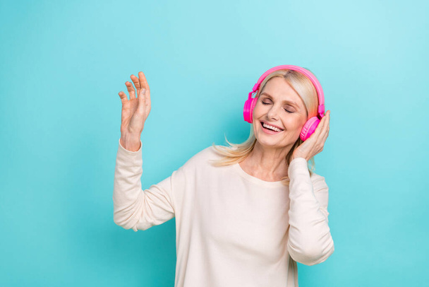 Photo of relaxed retired woman blonde hairstyle listen new sony headphones white shirt rhythm relax new soundtrack isolated on cyan color background. - Fotoğraf, Görsel