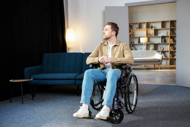 Positieve levensstijl, zorg voor gehandicapten, revalidatie en ondersteuning thuis. Jonge blanke man in rolstoel in woonkamer. - Foto, afbeelding