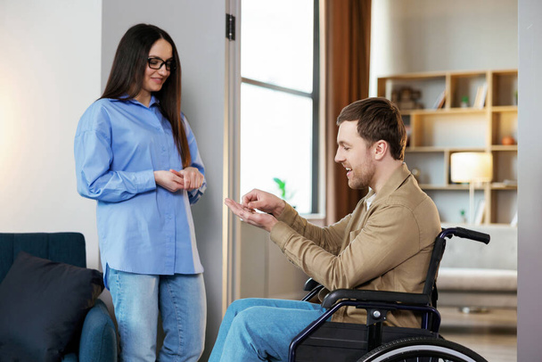 Een man in een rolstoel strekt haar handpalm uit. Vrouw geeft sleutel met sleutelhanger van nieuw huis voor gehandicapten. - Foto, afbeelding