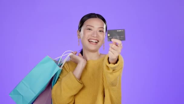 Nákupní taška, kreditní karta a úsměv s asijskou ženou ve studiu pro řešení, slevy a prodeje. Finance, propagace a platby s dívkou zákazníka za bohatství, produkt a nabídku na fialovém pozadí. - Záběry, video