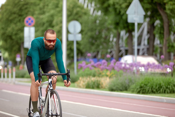 A cyclist man rides a bike in a city park along a bike path, a bicycle hobby, cycling around the city, cardio training on a bike. - Zdjęcie, obraz