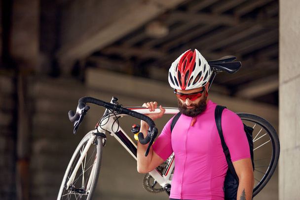 Pyöräilijä kuljettaa polkupyörää olkapäällään kaupungissa mies pyöräilyvaatteissa kypärä lasit ja puku polkupyörällä. - Valokuva, kuva