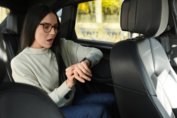 Емоційна жінка перевіряє час на годиннику в машині. Запізнення концепції
 - Фото, зображення