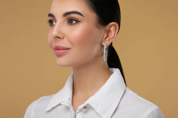 Beautiful young woman with elegant earrings on beige background, closeup - Фото, изображение