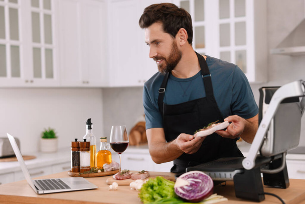 Man making dinner while watching online cooking course via laptop in kitchen - Fotó, kép