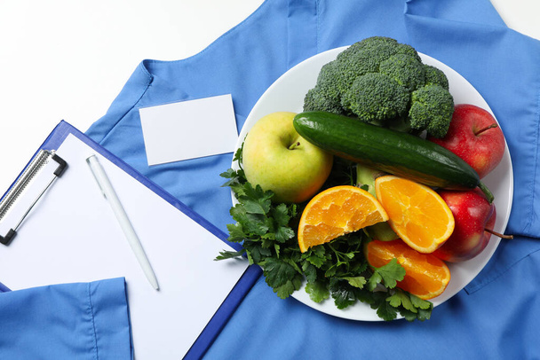 Uniforme de enfermeira e ferramentas, e comida saudável em fundo branco - Foto, Imagem