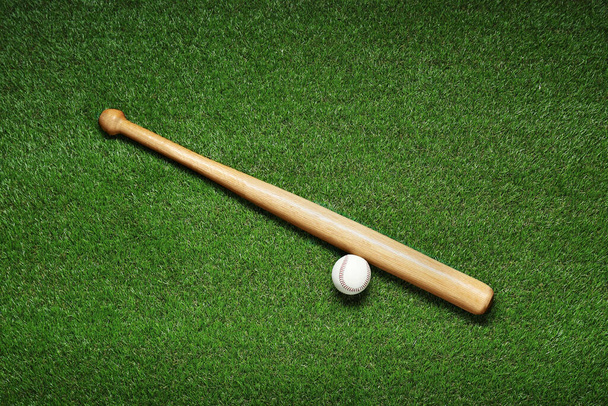 Wooden baseball bat and ball on green grass, flat lay. Sports equipment - Fotó, kép