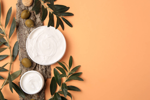 Flat lay composition with jars of cream and olives on pale orange background. Space for text - Foto, immagini