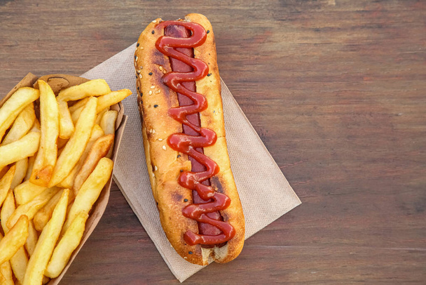 Fresh tasty hot dog and french fries on wooden table, flat lay. Space for text - Zdjęcie, obraz