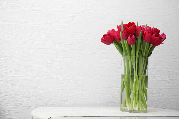 Bouquet of beautiful tulips in glass vase on table indoors. Space for text - 写真・画像