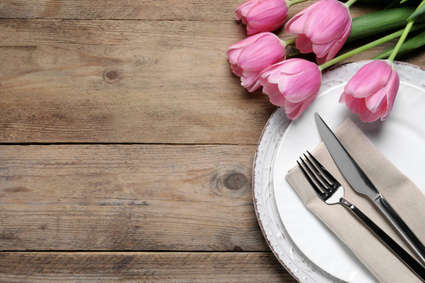 Stylish table setting with cutlery and tulips on wooden background, flat lay. Space for text - Zdjęcie, obraz