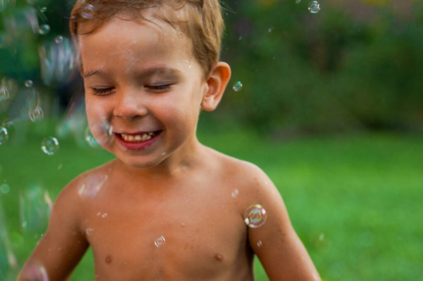 Um garotinho sem roupas está feliz em uma corrente de bolhas de sabão voadoras. - Foto, Imagem