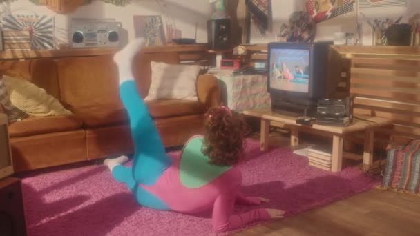Ευρύ πίσω μέρος του κοκκινομάλλα κορίτσι στη δεκαετία του ογδόντα αερόβια στολή άσκηση στο σαλόνι το απόγευμα, βλέποντας ταινία σε ρετρό τηλεόραση - Πλάνα, βίντεο