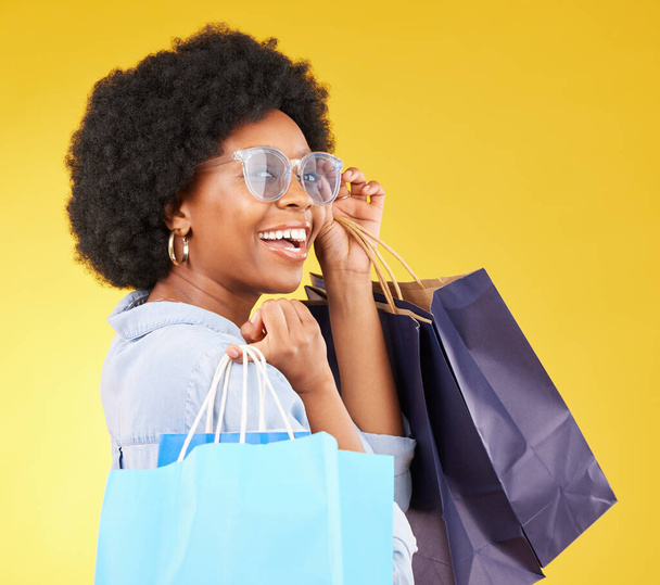 Bag, portrait and black woman shopping, excited and celebrating sale in studio on yellow background. Face, shopper and girl customer cheerful after boutique, retail or store discount posing isolated. - Foto, immagini