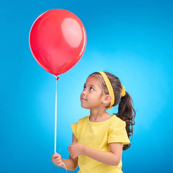 Young girl, studio and red balloon of a an kid alone ready for a birthday party to celebrate. Celebration event and female child holding balloons in the air with isolated blue background. - Photo, image