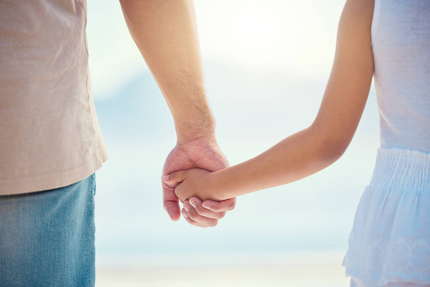 Holding hands, family or children with a father and daughter outdoor together at the beach during summer. Kids, love or trust with a man and female child standing outside for bonding during the day. - Photo, Image
