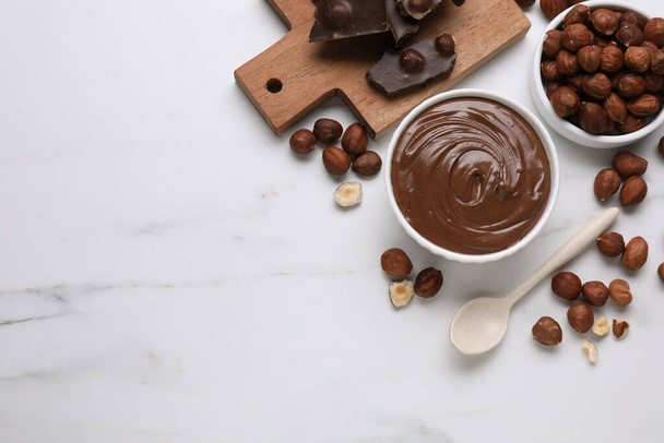 Bowl with tasty paste, chocolate pieces and nuts on white marble table, flat lay. Space for text - Photo, Image