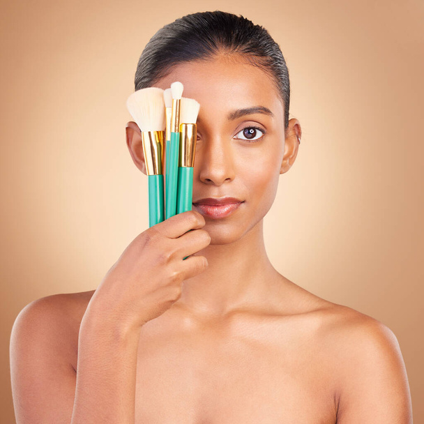 Makeup, cover and brush with portrait of Indian woman in studio for foundation, blush and self care. Glow, cosmetics and facial with female model on brown background for shine, clean and confidence. - Фото, изображение