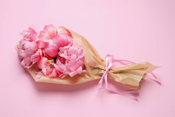 Beautiful bouquet of peonies wrapped in paper on pink background, top view - Foto, imagen