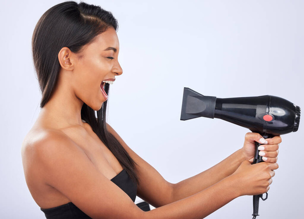Happy woman singing, hair care or dryer in studio for healthy natural shine, beauty or wellness. Funny Indian girl model, salon tools or self care equipment in grooming routine on white background. - Foto, immagini