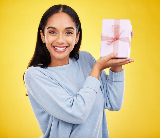 Woman smile, portrait and gift box in a studio happy from surprise present for birthday. Giveaway prize, isolated and yellow background of a young female student feeling positive and cheerful. - Foto, Imagem