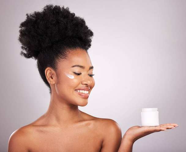 Black woman, moisturizer cream and smile for skincare beauty or cosmetics against a gray studio background. Happy African female smiling and holding moisturizing creme, lotion or facial product. - Photo, Image