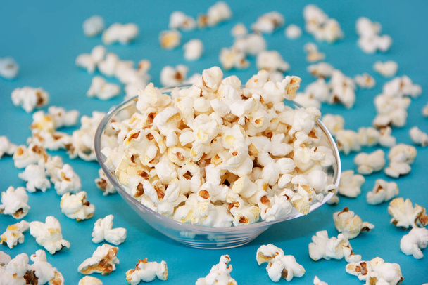 White fried popcorn in a transparent glass plate on a blue background - Фото, изображение