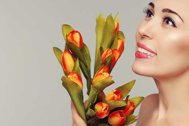 Spring Beauty Model Studio Shooting. Porträt einer lächelnden Frau mit Blumen orange gelbe Tulpen auf weißem Hintergrund. Mode frisches Make-up. Sinnliche Lippen. perfekte Haut. Zärtlichkeit. Romantischer Stil. - Foto, Bild