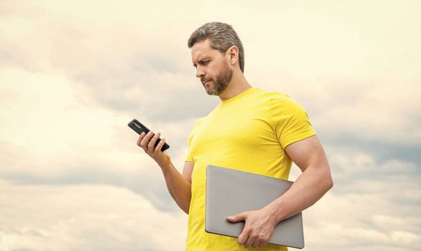 man with pc chatting on smartphone on sky background. - Φωτογραφία, εικόνα