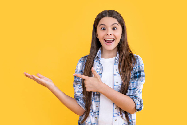 photo of surprised teen girl with long hair wearing checkered shirt. teen girl isolated on yellow. teen girl in studio. teen girl on background. - Foto, afbeelding