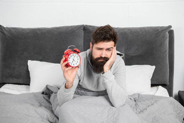 Sleepy guy holding alarm clock being in bed in morning, time. - Foto, Bild