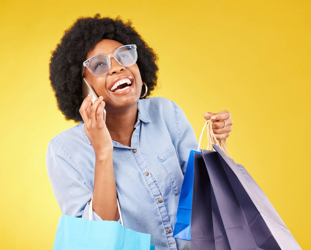Shopping bag, phone call communication or black woman with sales product, discount fashion deal or mall store present. Talking, designer gift or chic happy customer chat isolated on yellow background. - 写真・画像