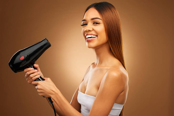 Hair, hairdryer and smile portrait of woman in studio for growth, color or healthy texture. Aesthetic female hands with heat for haircare, self care and hairdresser or beauty salon brown background. - Valokuva, kuva